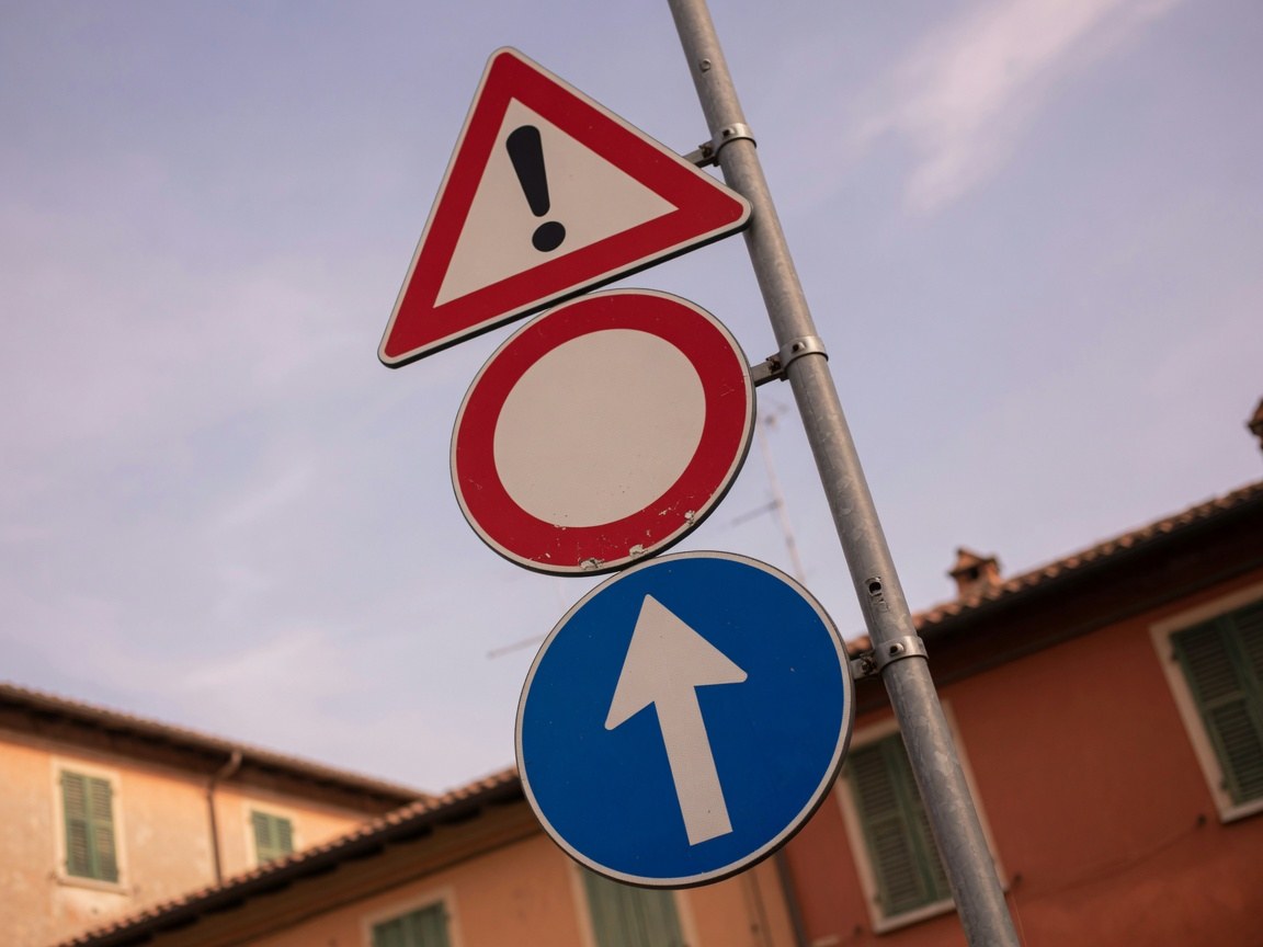 Segnale di curva pericolosa e limite 50 su una strada toscana alberata di cipressi